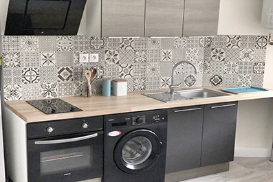 Cuisine équipée d'un studio : crédence carreaux de ciment, plaque, four et lave-linge.
