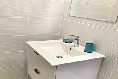 Salle de bain d'un studio : meuble vasque blanc, faïence claire et miroir.