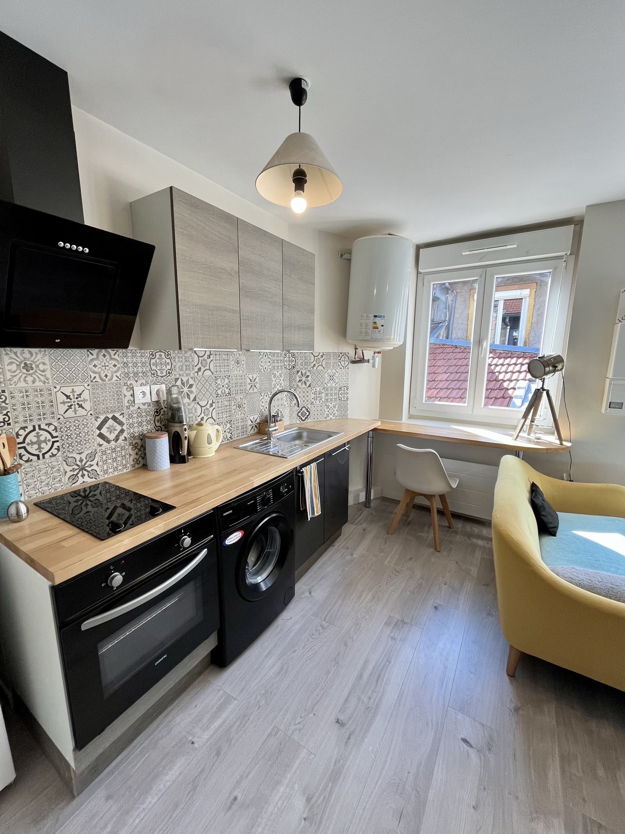 Cuisine d'un studio avec plan de travail bois, crédence carreaux de ciment et fauteuil jaune moutarde.