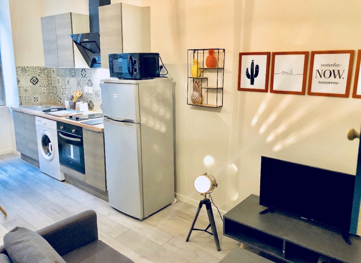 Coin salon d'un studio avec TV écran plat, cadres décoratifs et cuisine équipée attenante.