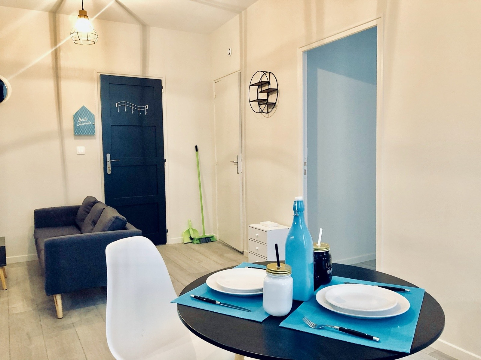 Entrée d'un studio meublé avec porte bleu canard, canapé et table dressée.